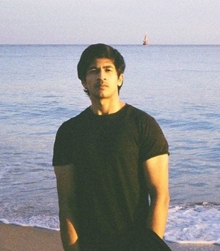 Ayush Patel on a beach at golden hour with the sea behind
