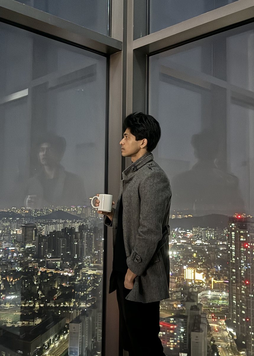 Ayush Patel with a coffee overlooking the Cheonan city skyline at night from a high-rise