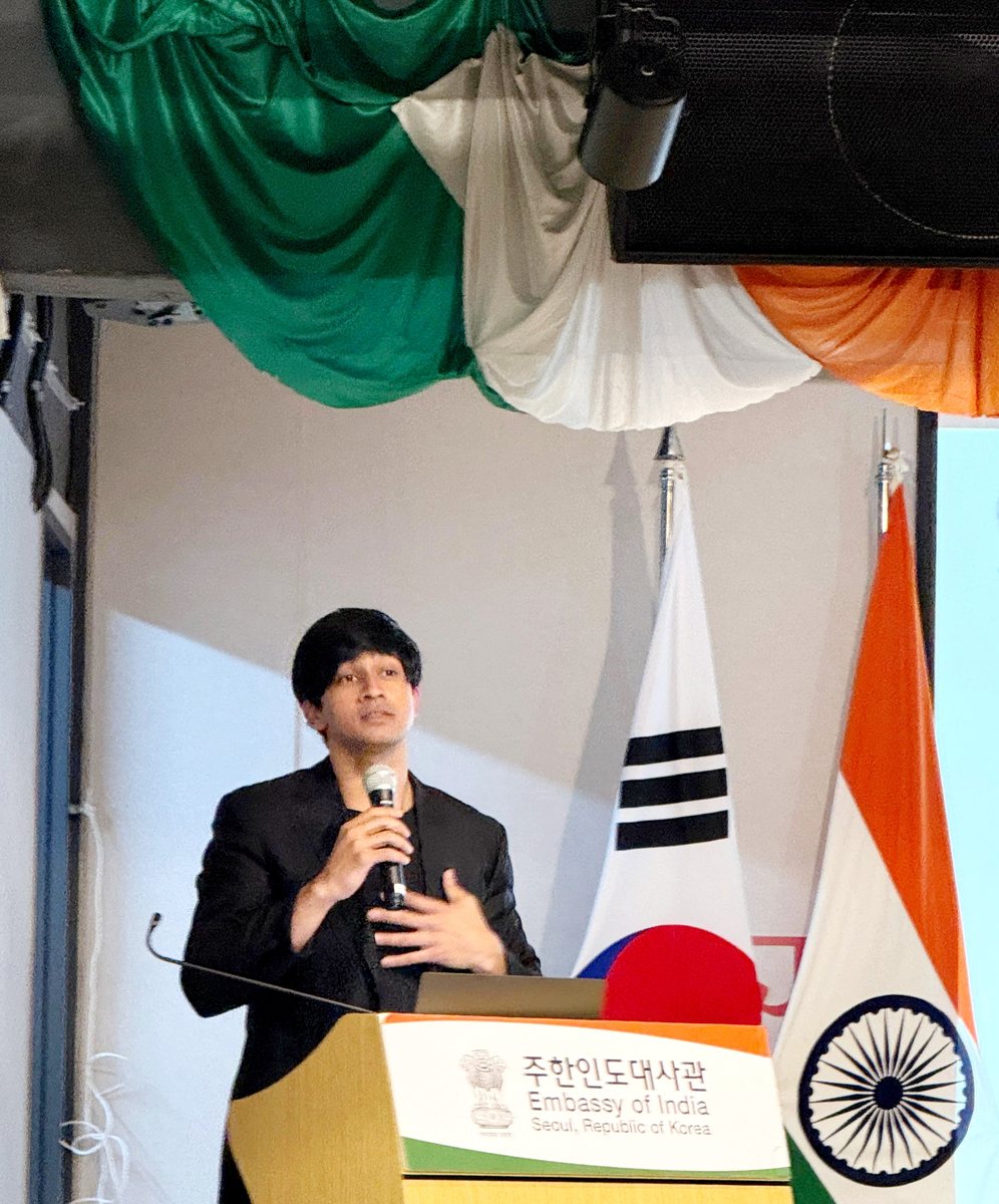 Ayush Patel speaking at the Embassy of India, Seoul, with the Indian and Korean flags beside the podium